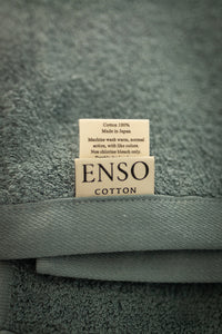 Folded towel with 'ENSO COTTON' label on a textured gray background