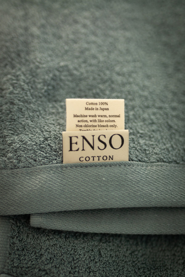 Folded towel with 'ENSO COTTON' label on a textured gray background