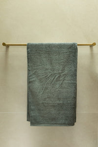 Green towel hanging on a gold towel rack against a beige wall.