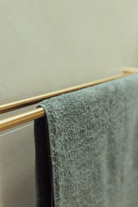 Green towel hanging on a gold towel rack against a beige wall.