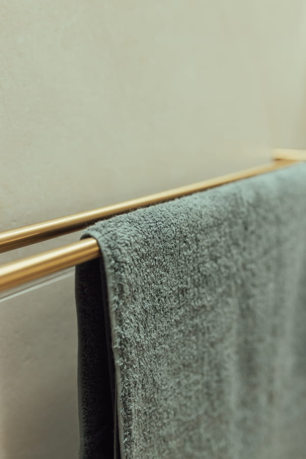 Green towel hanging on a gold towel rack against a beige wall.