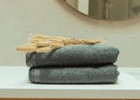 Stack of folded towels on a surface with decorative wheat stalks, against a neutral background.