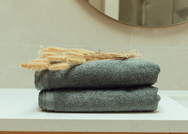 Stack of folded towels on a surface with decorative wheat stalks, against a neutral background.