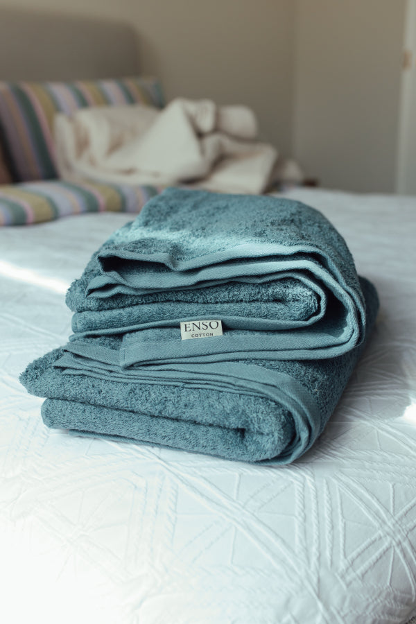 Folded teal blanket with 'ENSO' label on a bed