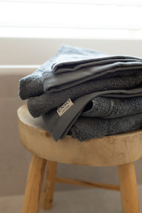 Stack of gray towels on a wooden stool with a blurred bathtub background