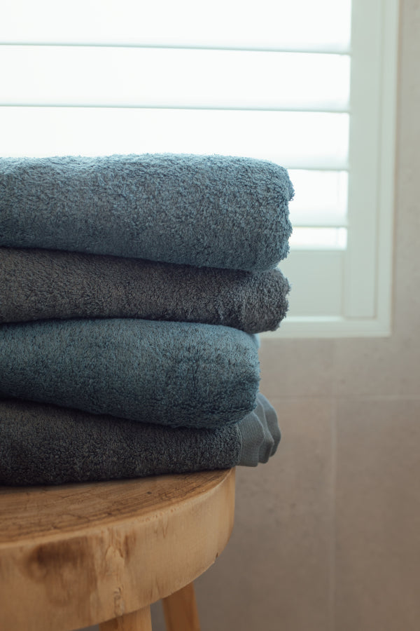 Stack of folded towels on a wooden stool with a neutral background