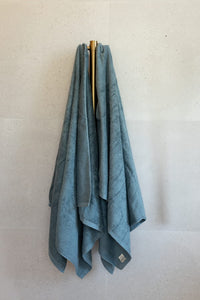 Blue towel hanging on a gold hook against a white wall