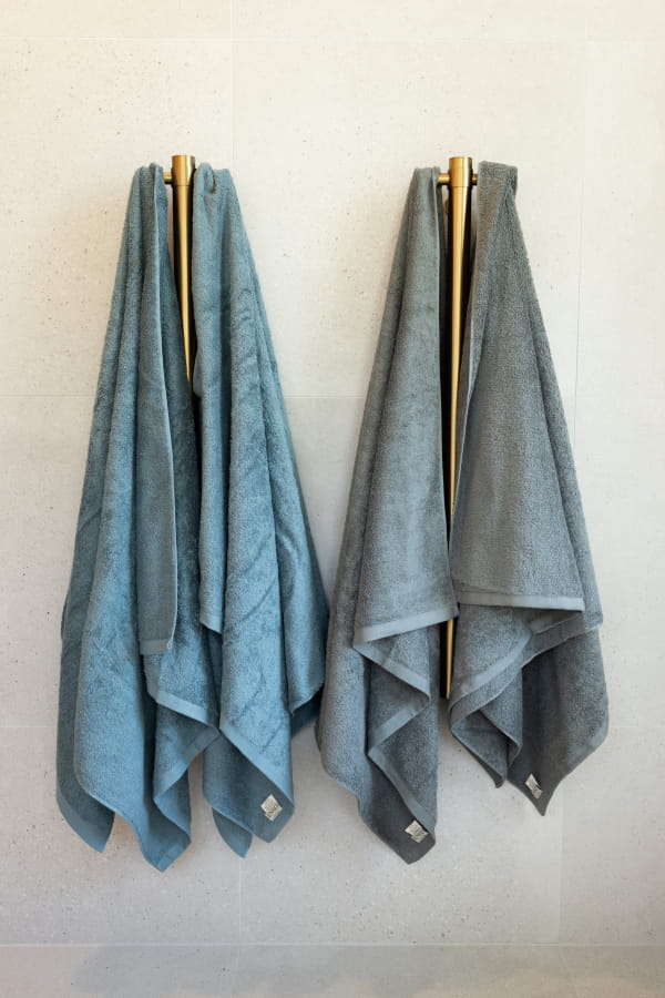 Two blue towels hanging on wooden racks against a white wall.
