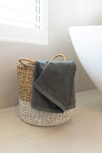 Wicker basket with a gray towel on a white surface, possibly a bathroom setting.