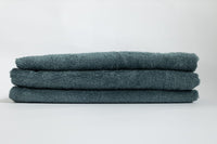 Stack of three folded teal towels on a white background