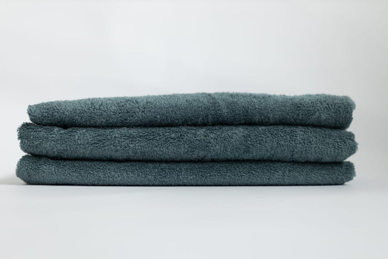Stack of three folded teal towels on a white background